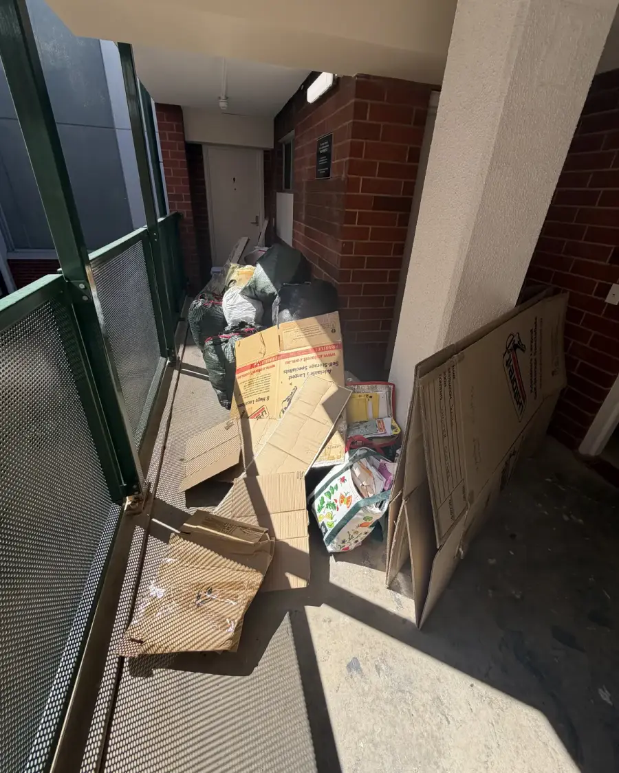 Before: Boxes and rubbish piled along a unit balcony walkway