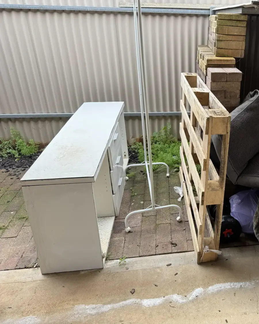 Before: Pallets, a white cabinet and household items in a backyard lean-to