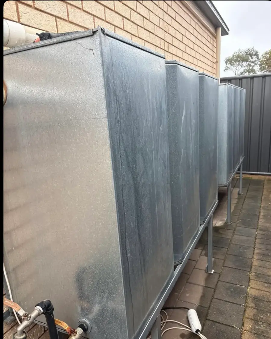 Before: Row of old galvanised water tanks on stands along a brick wall